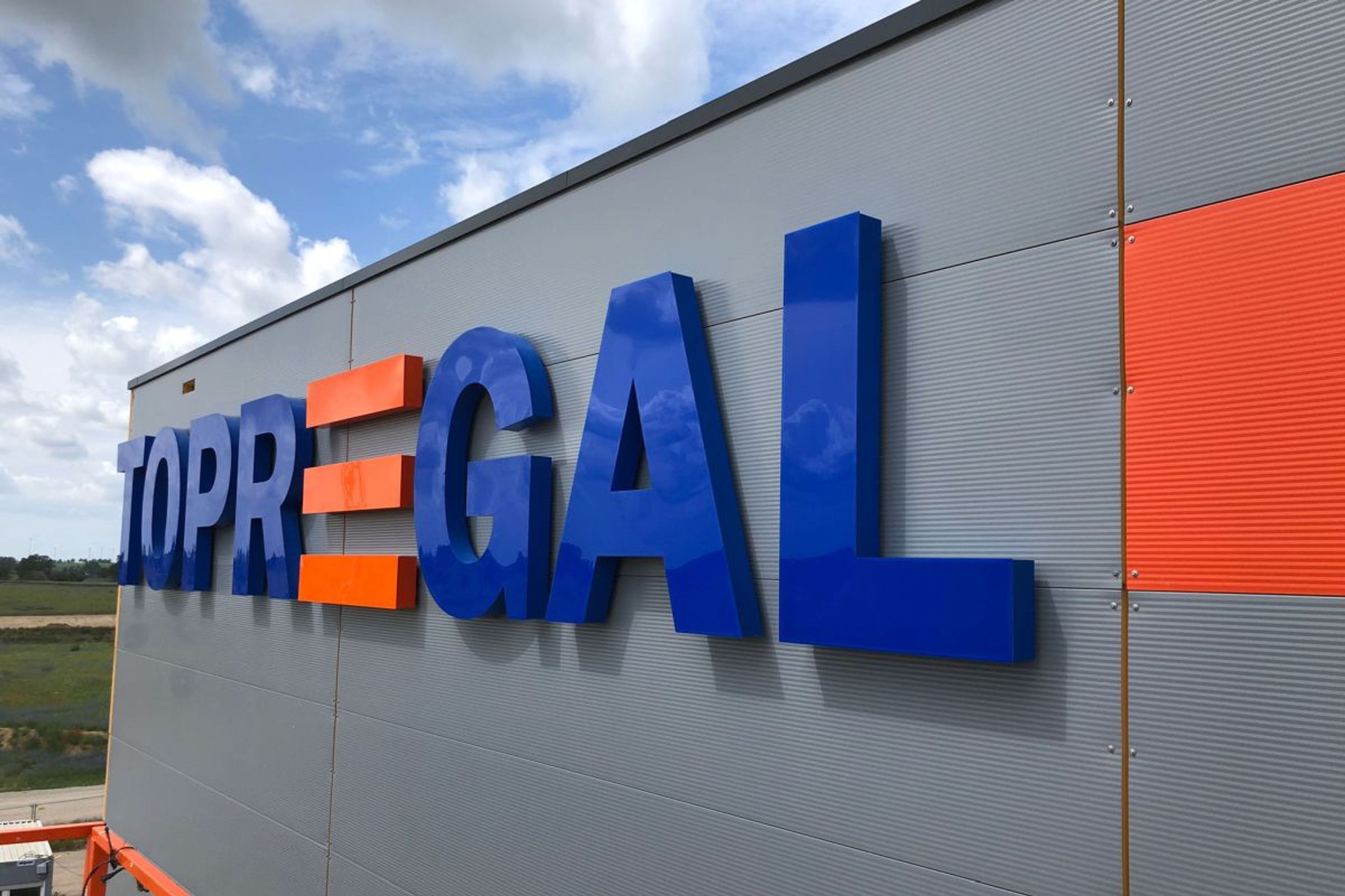 Große blaue und orange Buchstaben an der Fassade einer Halle, bei Tag