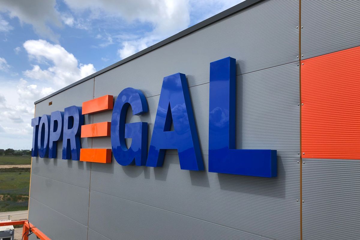 Große blaue und orange Buchstaben an der Fassade einer Halle, bei Tag