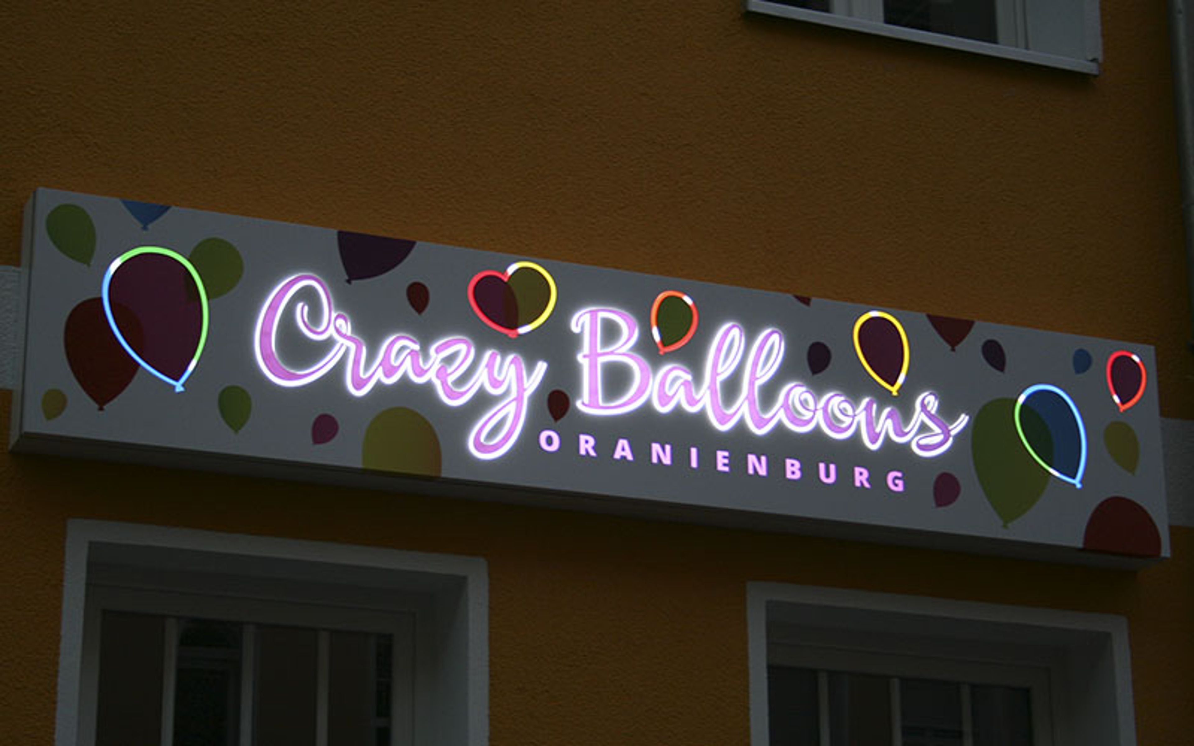 Leuchtkasten mit Schreibschrift und Ballon-Motiven an einer Fassade