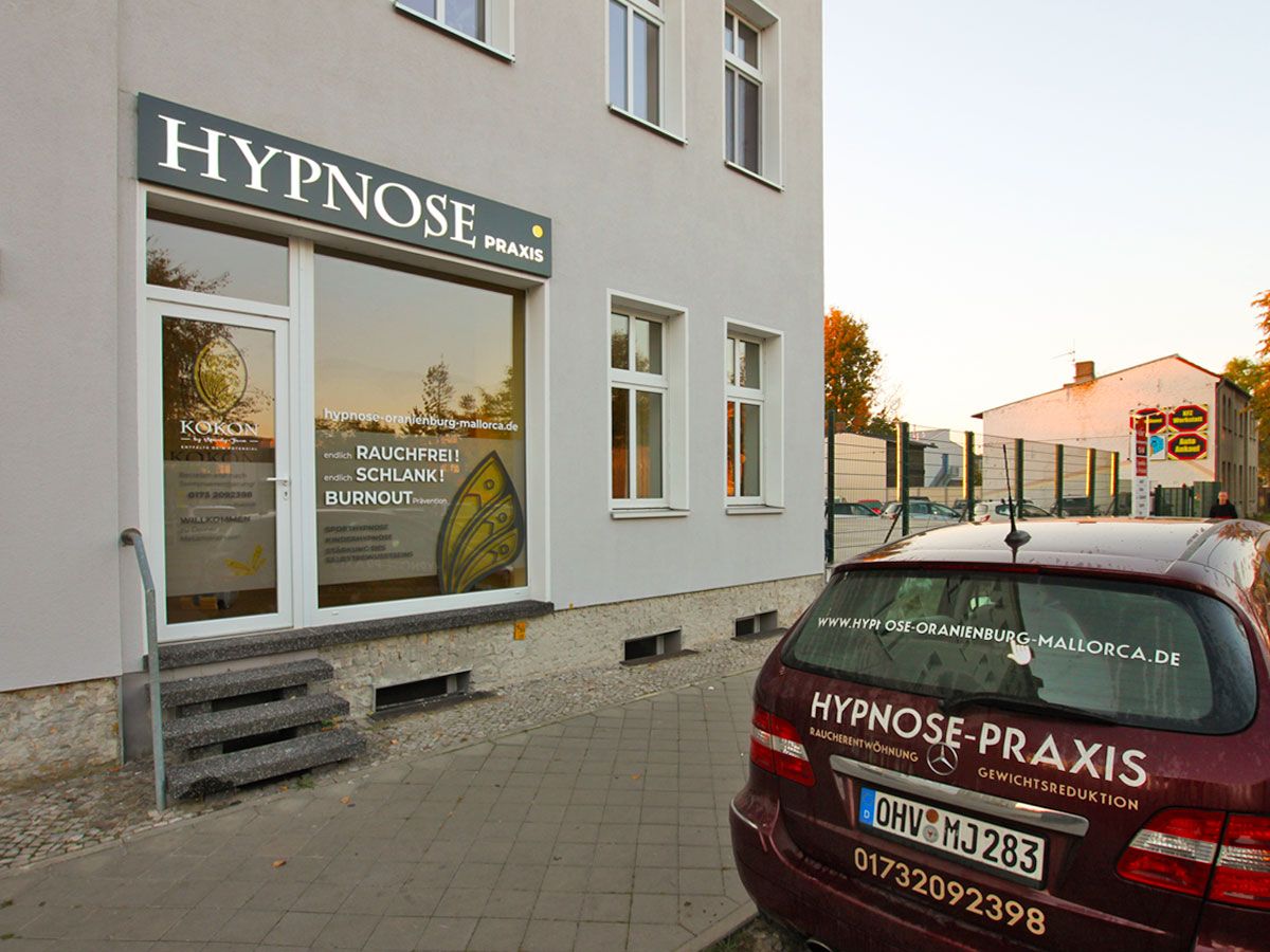 Leuchtkasten mit heller Schrift über Eingang und Schaufenster einer Praxis