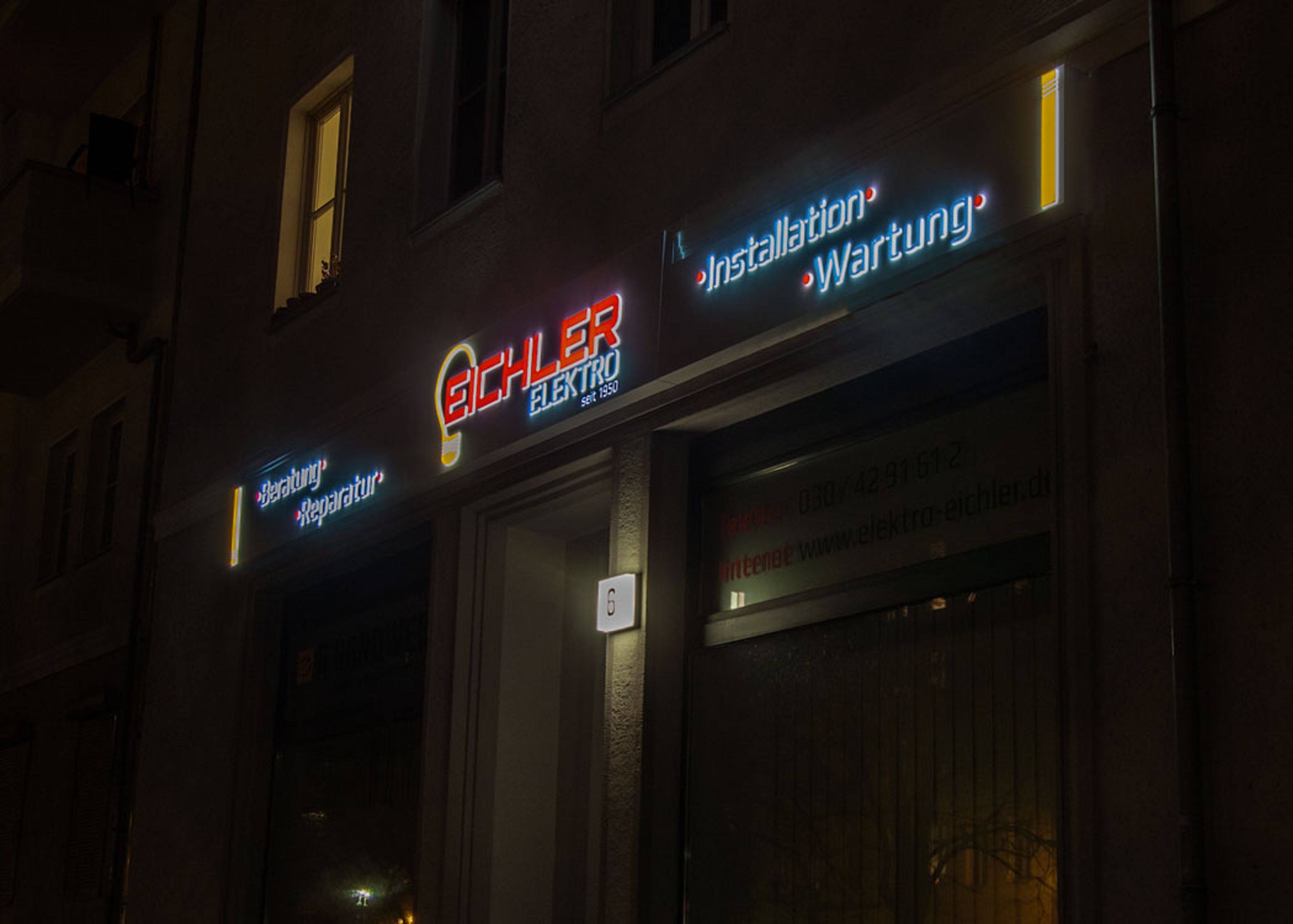 Leuchtkasten mit leuchtender Schrift über einem Ladengeschäft bei Nacht, schräg von der Seite