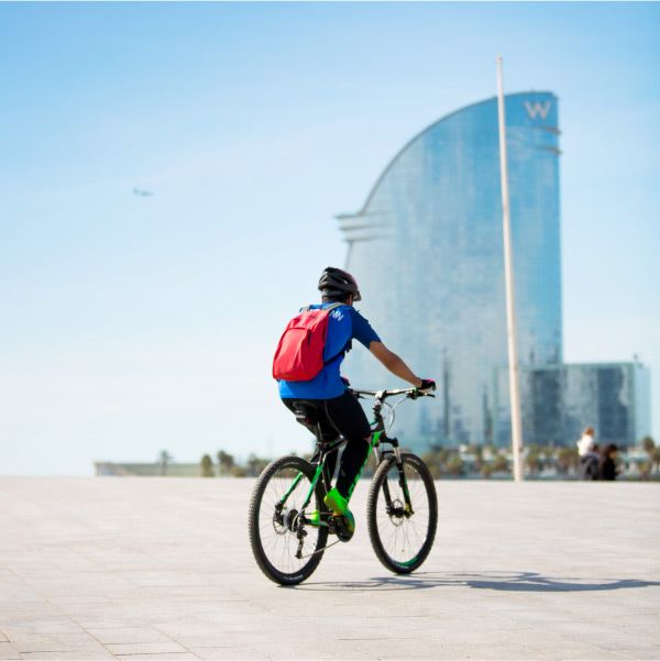 Hombre de espaldas montado en una bici con el Hotel Vela de Barcelona de fondo