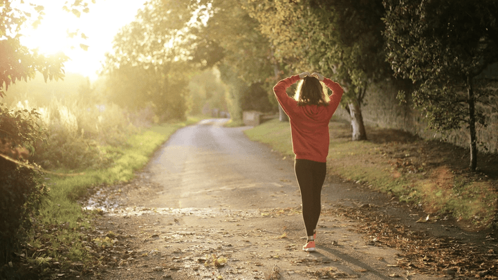 Mujer de espaldas en un camino entre árboles calentando antes de correr