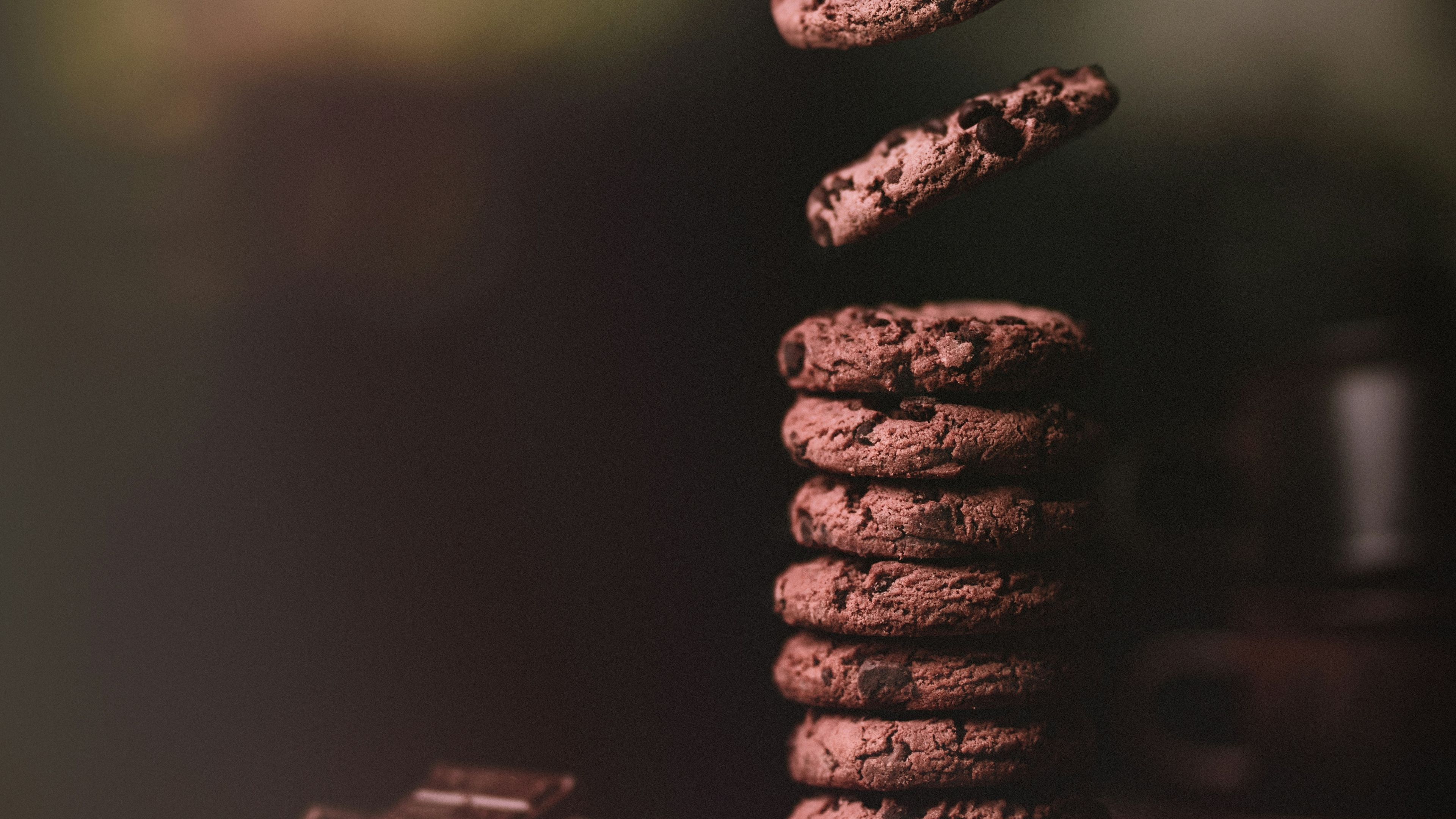 Chocolate chip cookies falling into a stack on a wooden chopping board