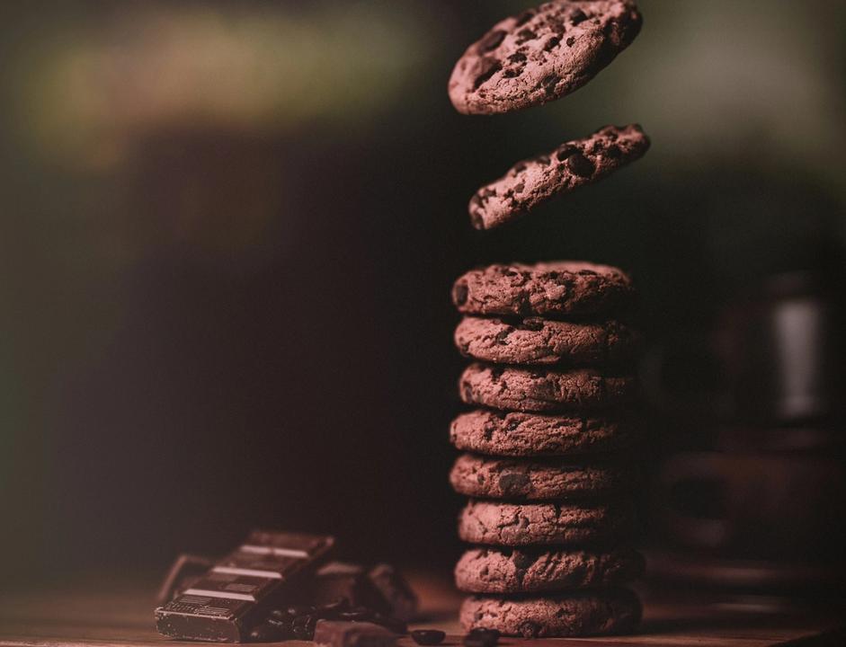 Chocolate chip cookies falling into a stack on a wooden chopping board