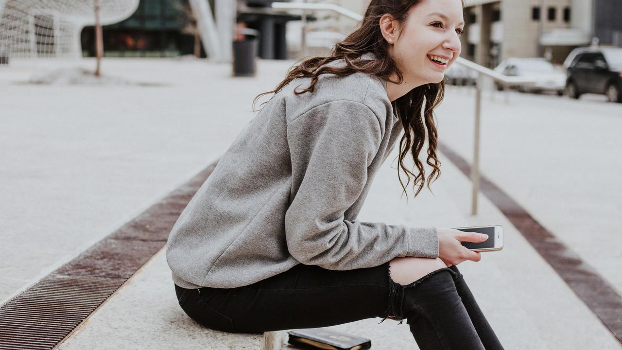 Woman smiling sitting on a ledge holding a smartphone