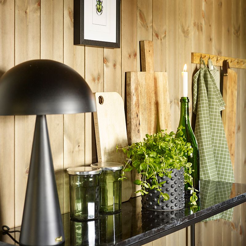 Kjøkkenhylle med lampe, urter og skjærefjøl. Beiset panel på veggen