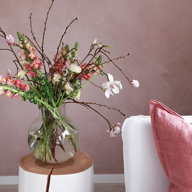 flott blomsterbukett i glassvase står på et sidebord ved siden av en hvit sofa