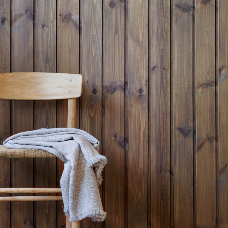 en stol med et pledd på står foran en brunbeiset vegg