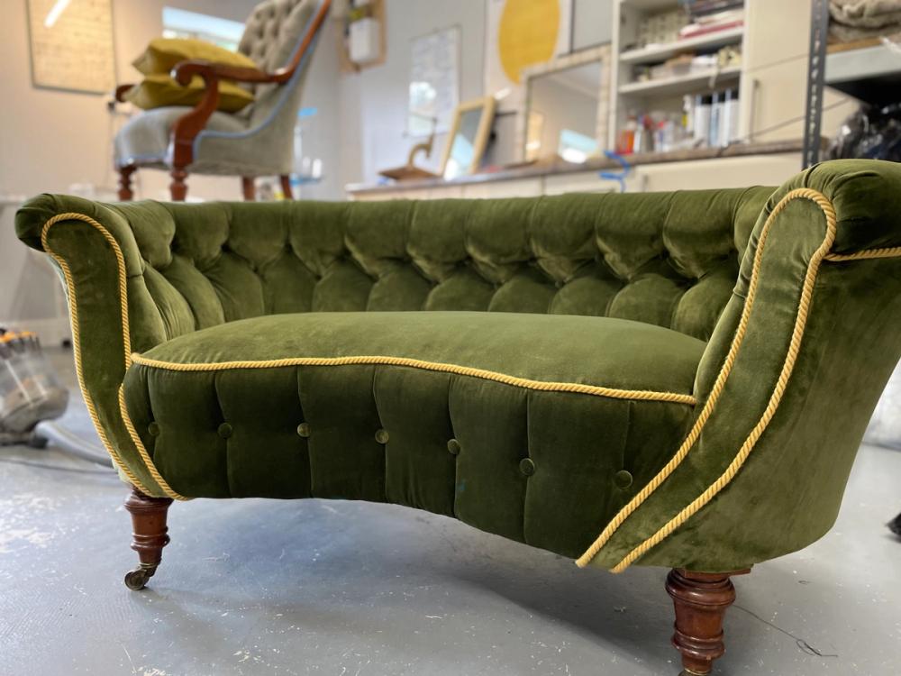 A two seater rounded button back sofa in a green velvet with gold trim,  viewed from the front