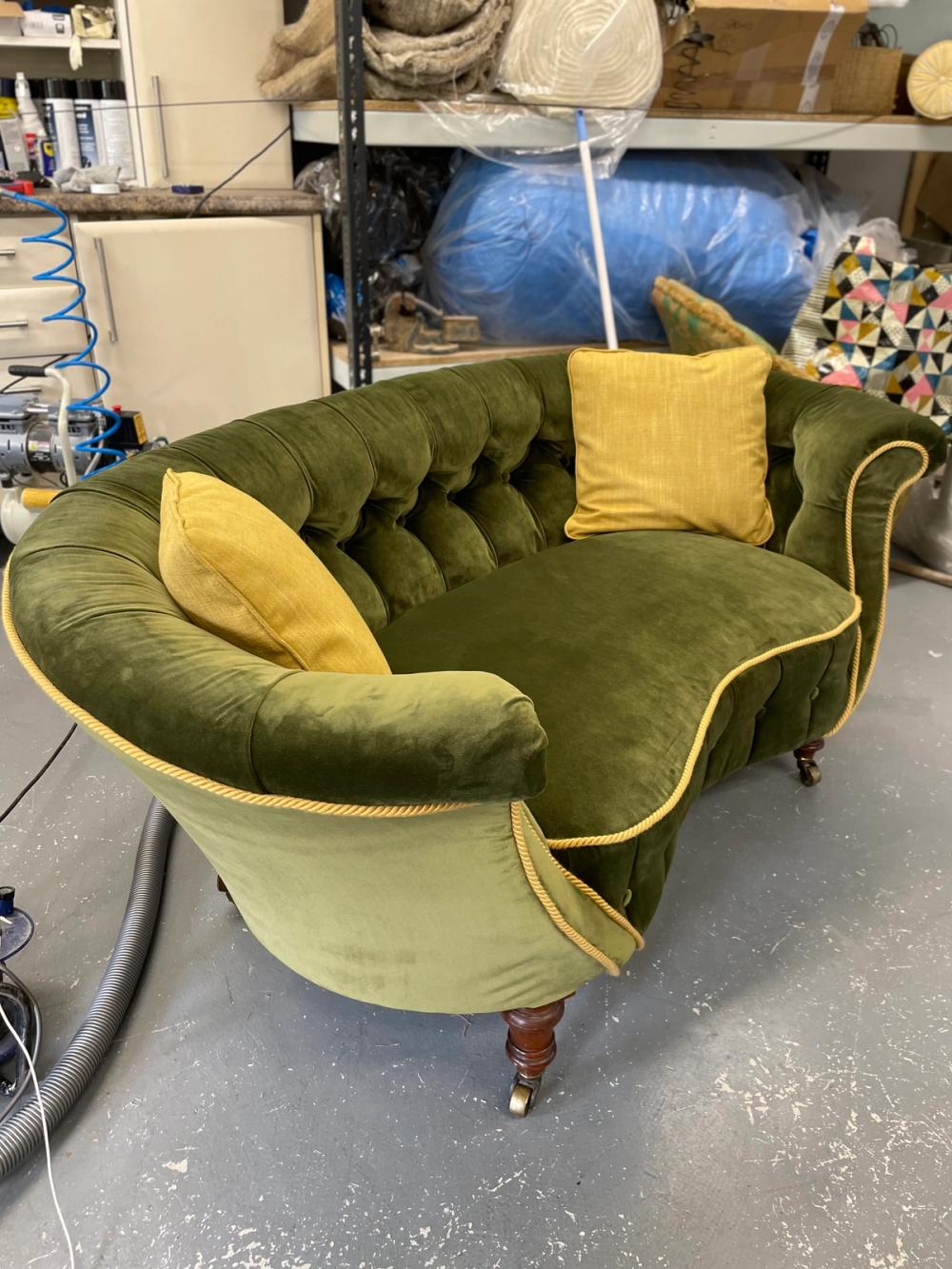 A two seater rounded button back sofa in a green velvet with gold trim, viewed from the side