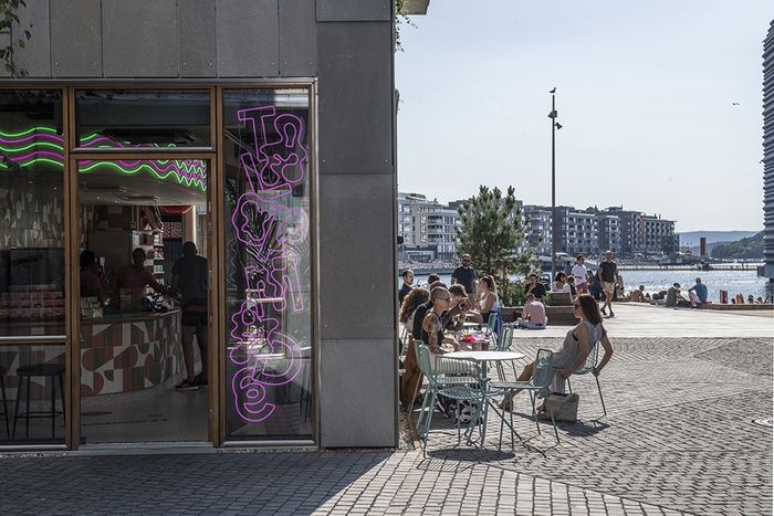 Folk sitter på en uteservering ved fjorden på en varm sommerdag.