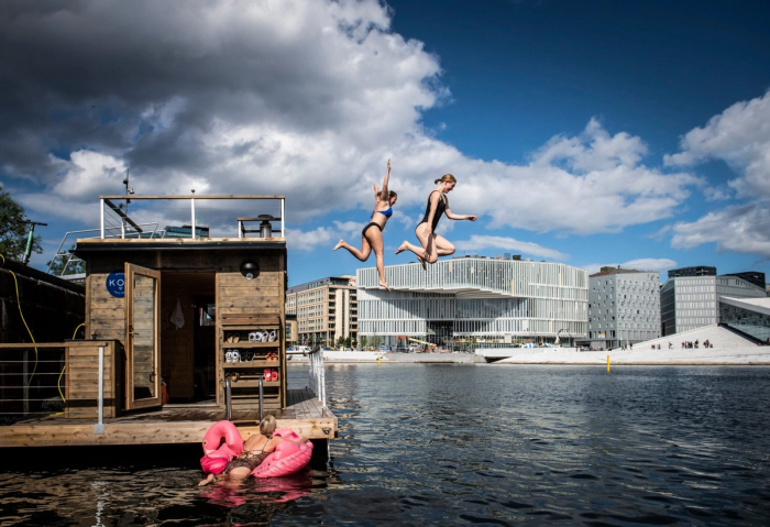 Tre jenter bader og hopper i havet rett ved Operaen og Deichman i Bjørvika.