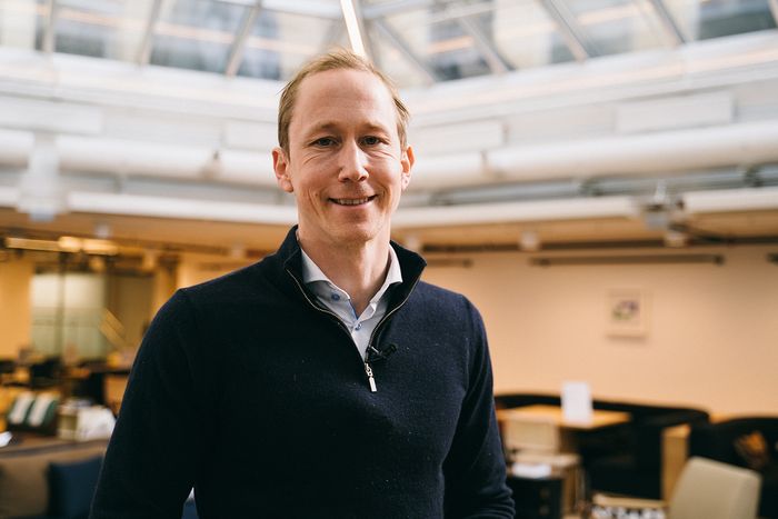 Henrik Botten Taubøll snakker om framtidens kontormarked. Han står i et kontorlandskap og smiler til kamera med mikrofonmygg på genseren.