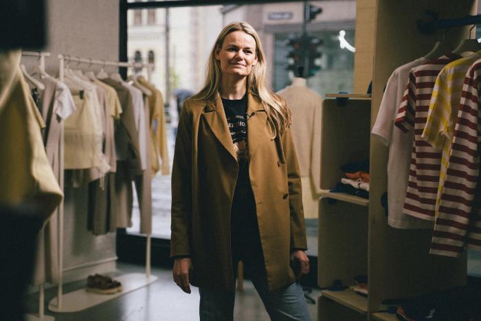 Susanne Holzweiler snakker om retailtrender etter pandemien. Hun har lyst langt hår og står inne i en klesbutikk med opphengte klær rundt seg.