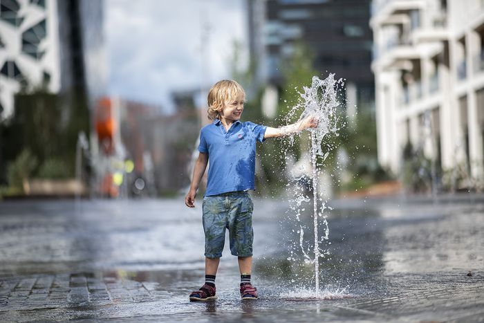 En lyshåret gutt på ca. 5 år leker med vann fra en fontene. 