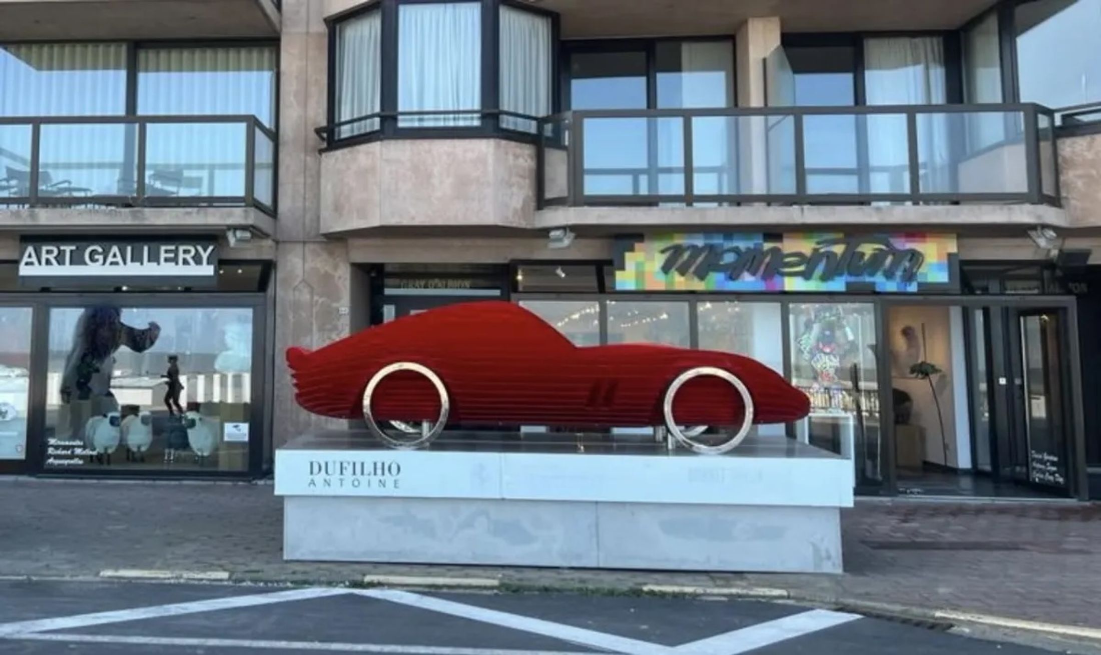 A sculpture of a red car in front of an art gallery