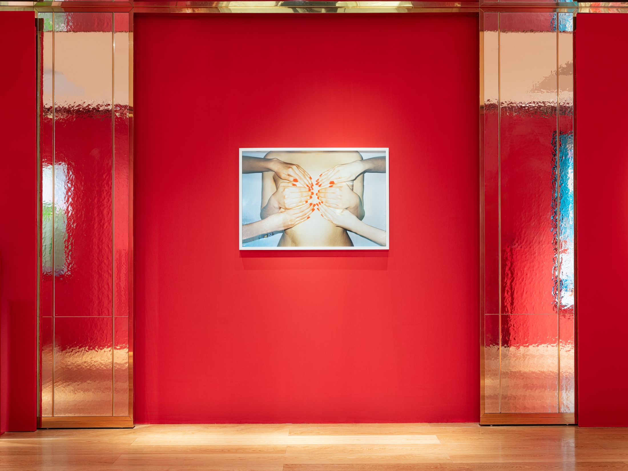 A photo on a red wall of hans covering a woman's chest