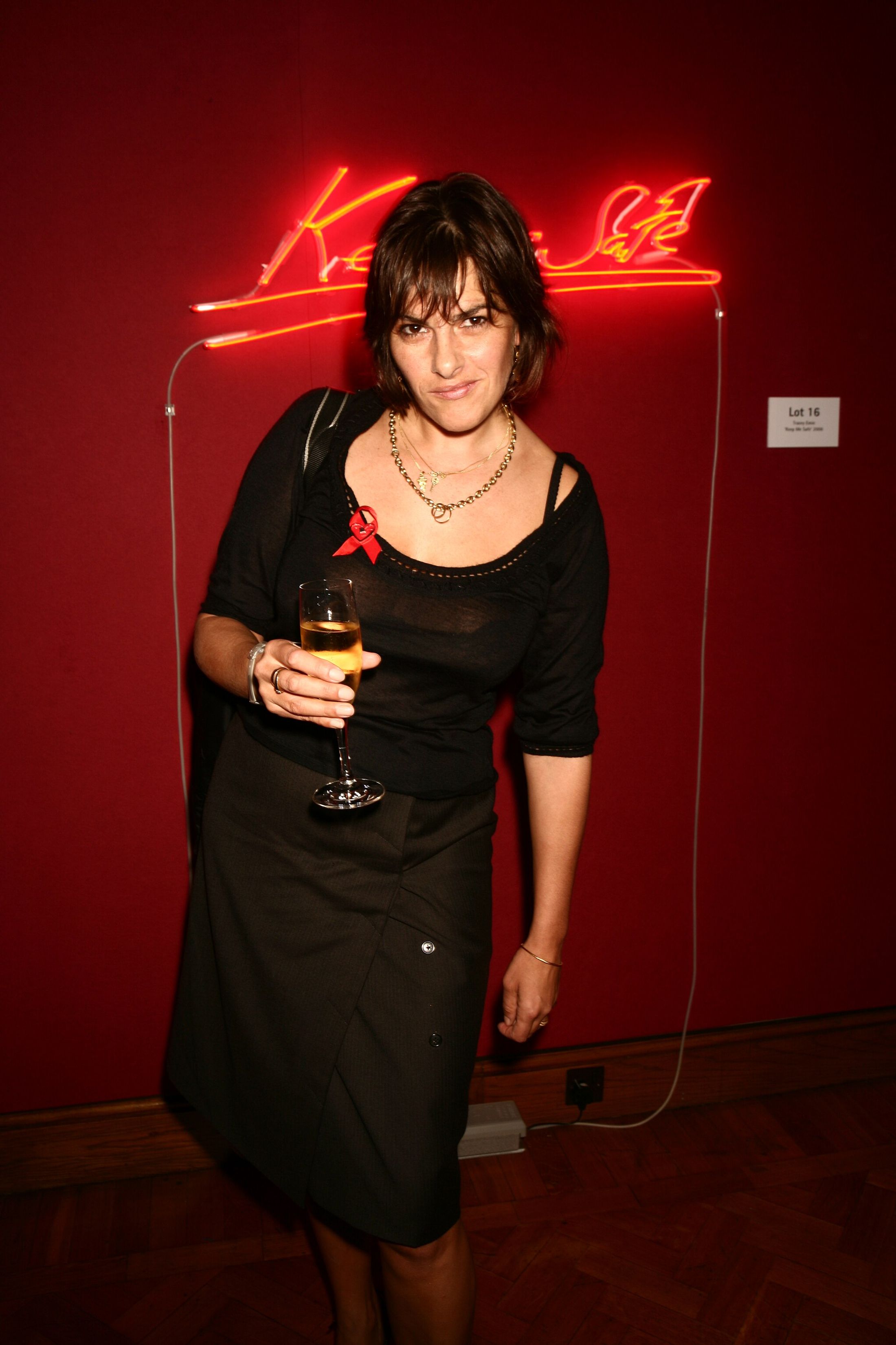 A woman holding a glass of wine wearing black in front of a red background