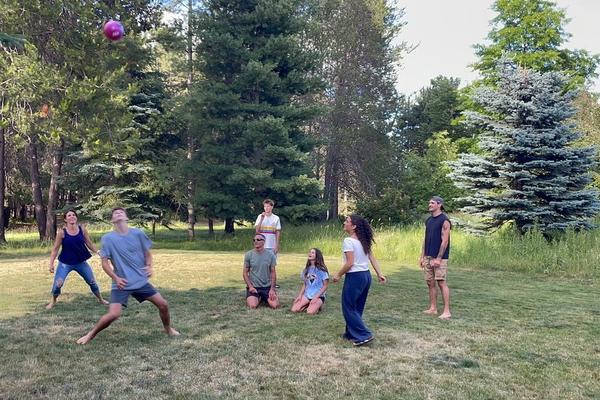 Family playing an outdoor game with a volleyball with a couple sitting in the middle and the rest standing in a circle.