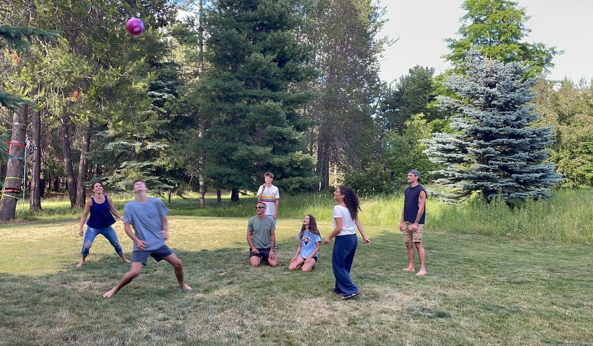 Family playing an outdoor game with a volleyball with a couple sitting in the middle and the rest standing in a circle.