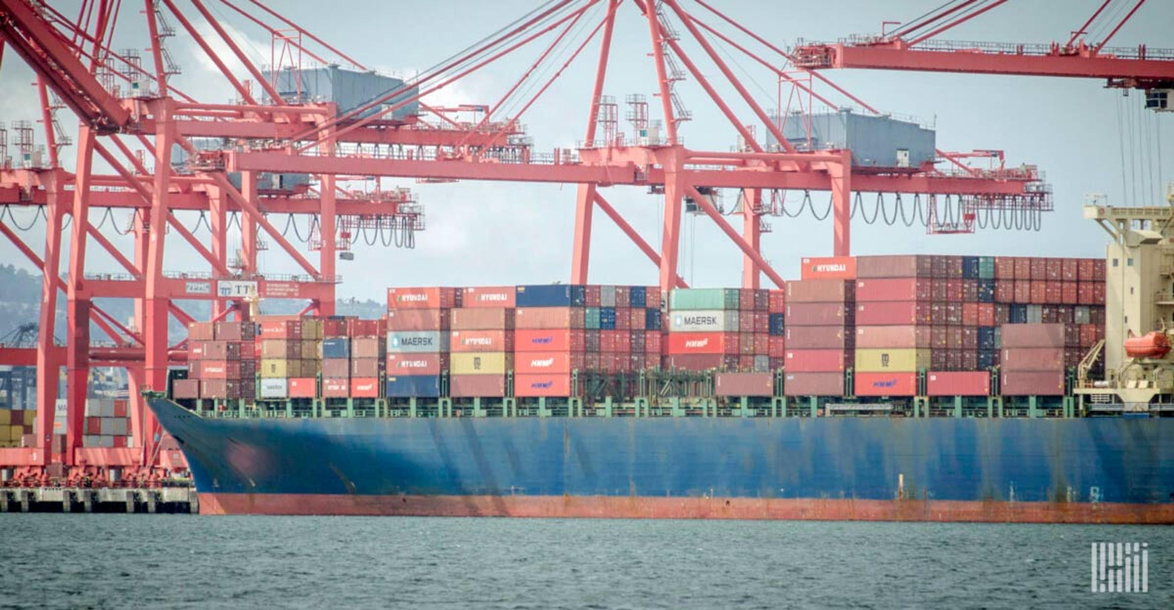A blue vessel docked at a port with multiple containers on it