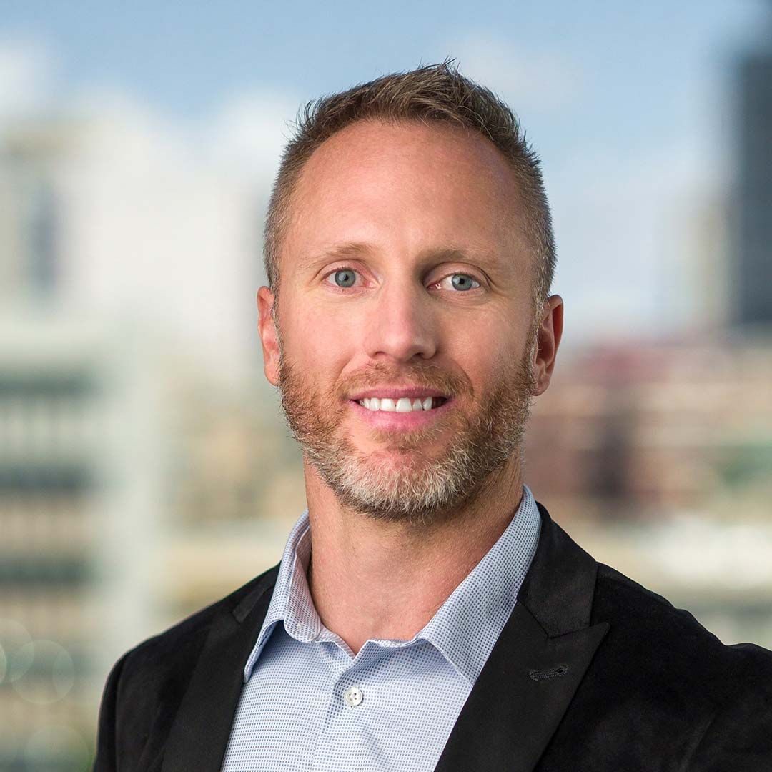Smiling man with a blue shirt and black coat.