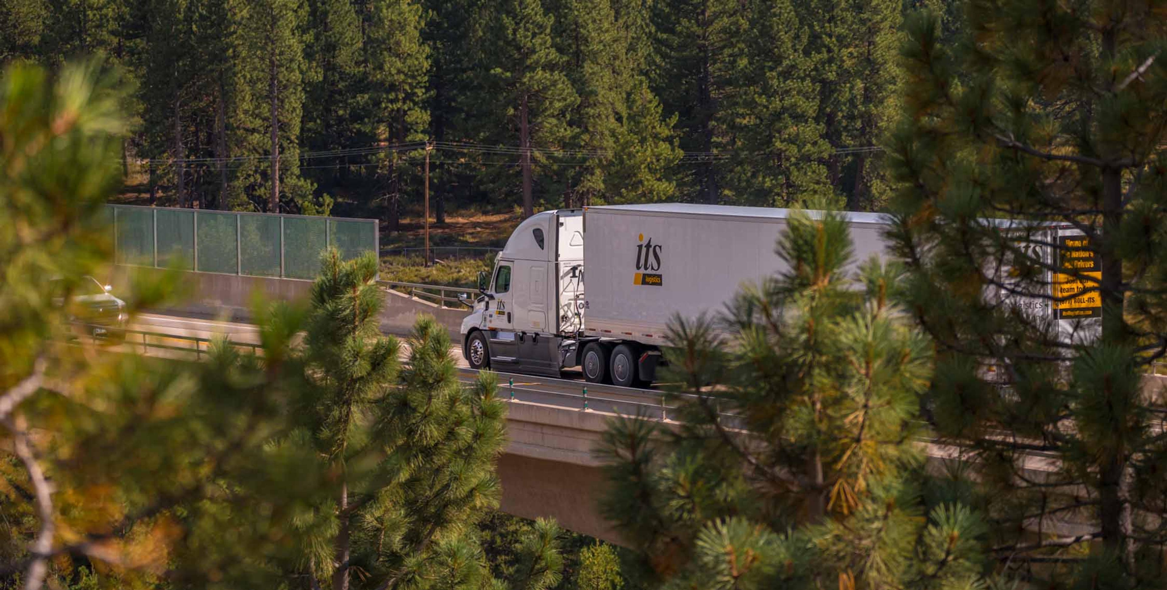 ITS truck driving on the freeway surrounded by lots of trees
