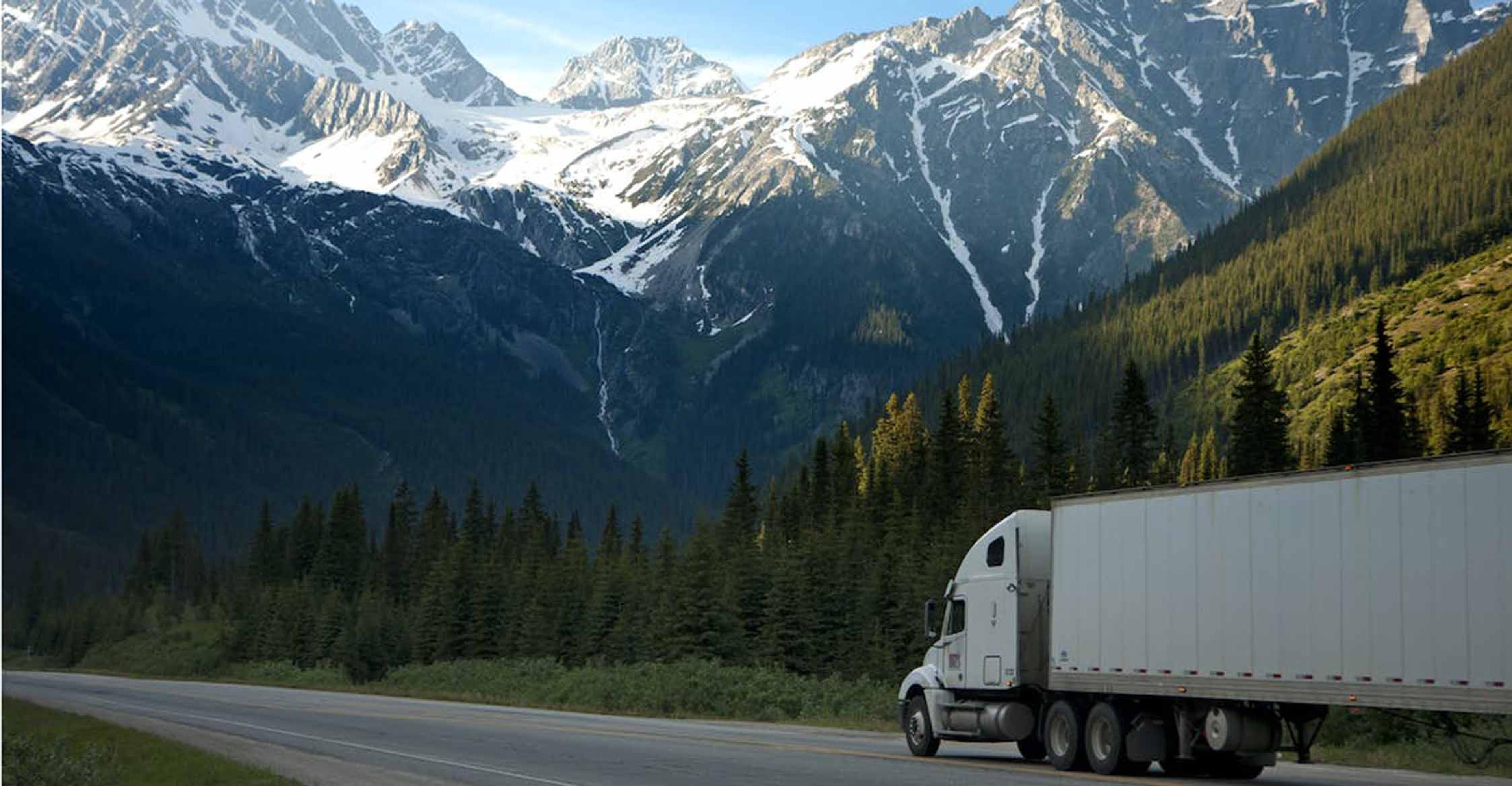 truck driving down road with mountains in backround