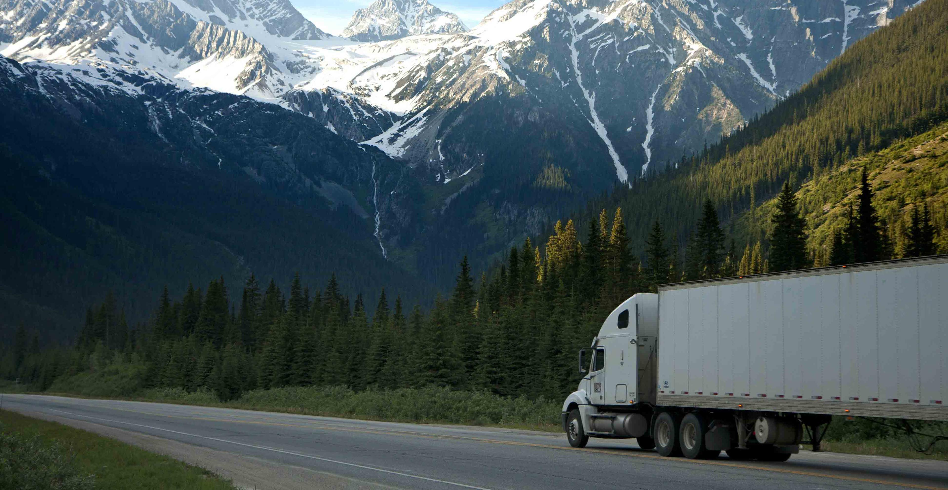 A white truck driving on the road with mountains in the background