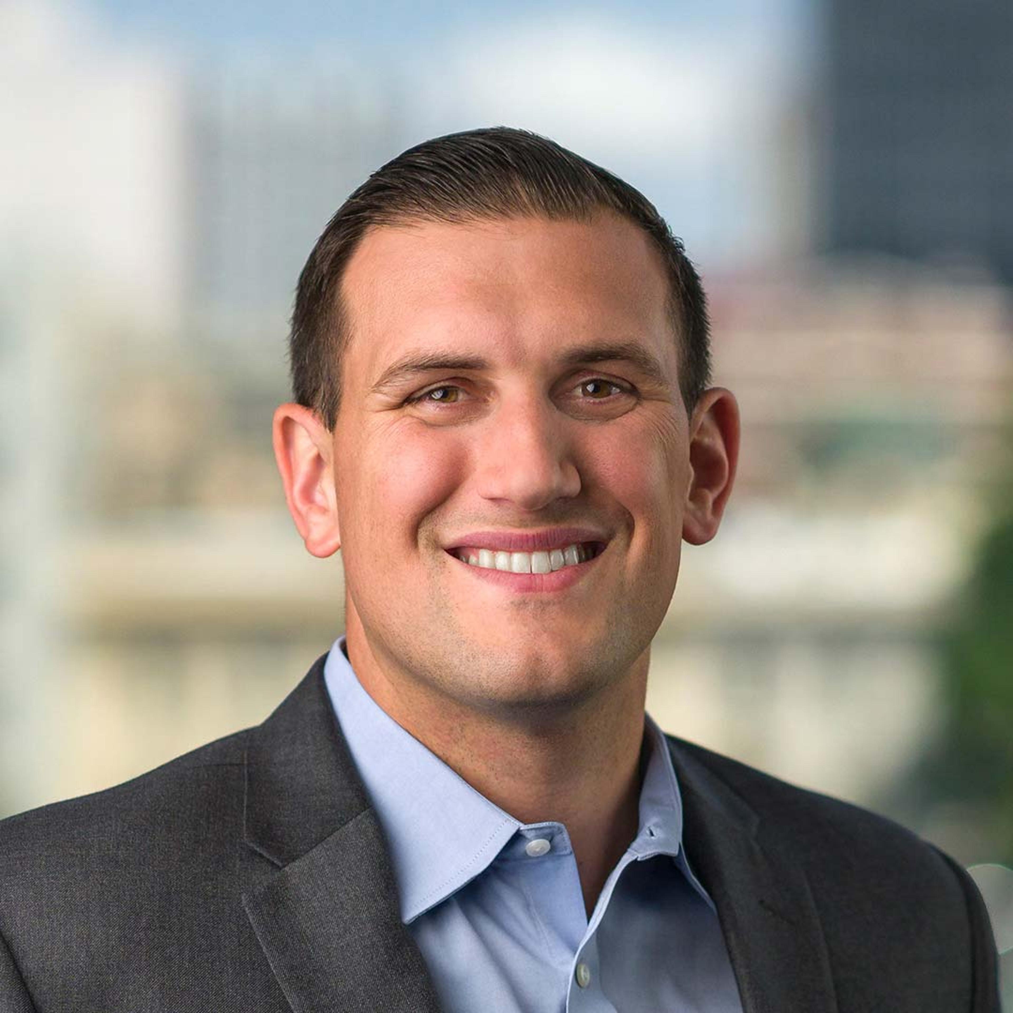 Smiling man with a blue shirt and black coat.