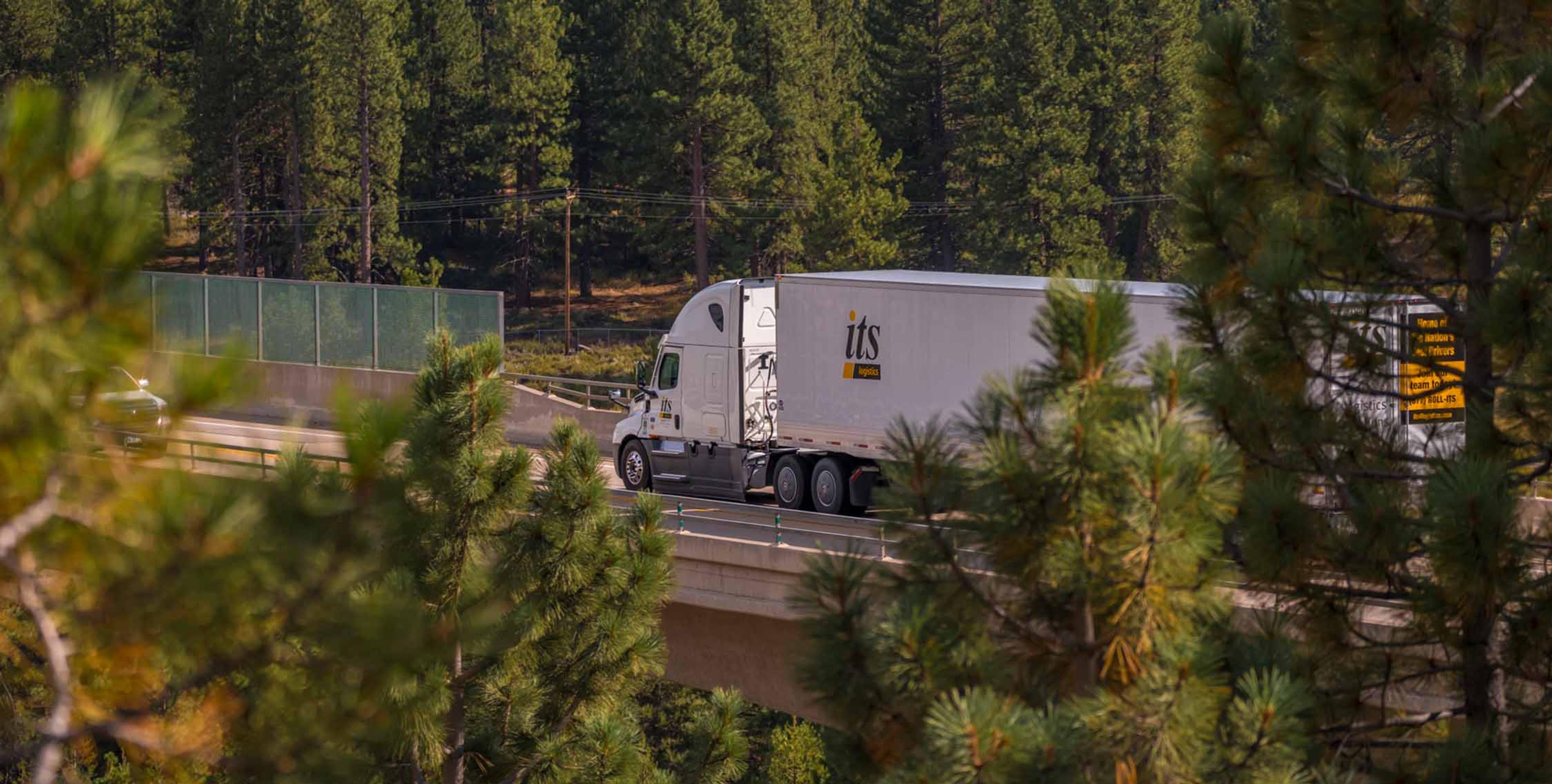 ITS truck driving on the freeway surrounded by lots of trees