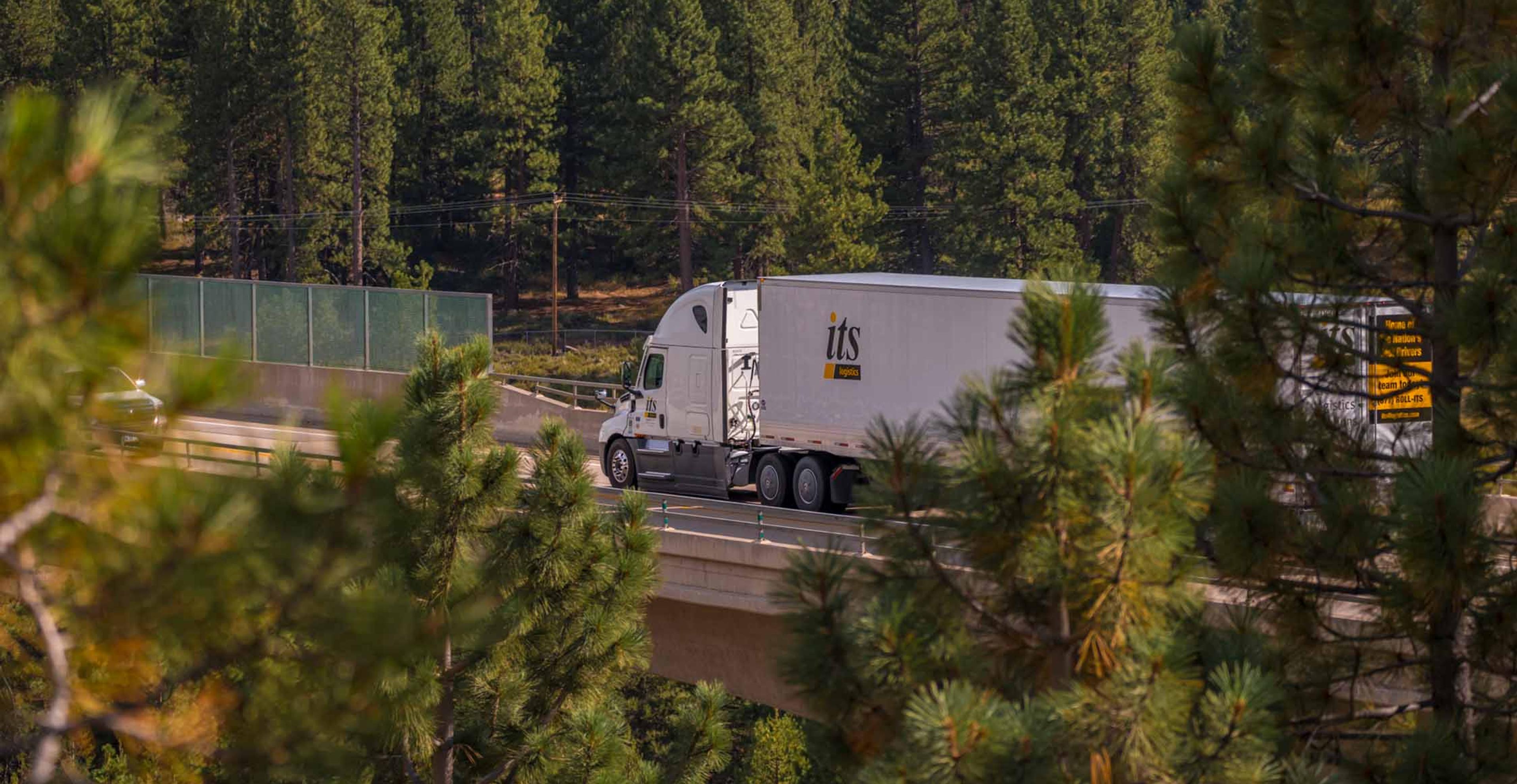 ITS truck driving on the freeway surrounded by lots of trees