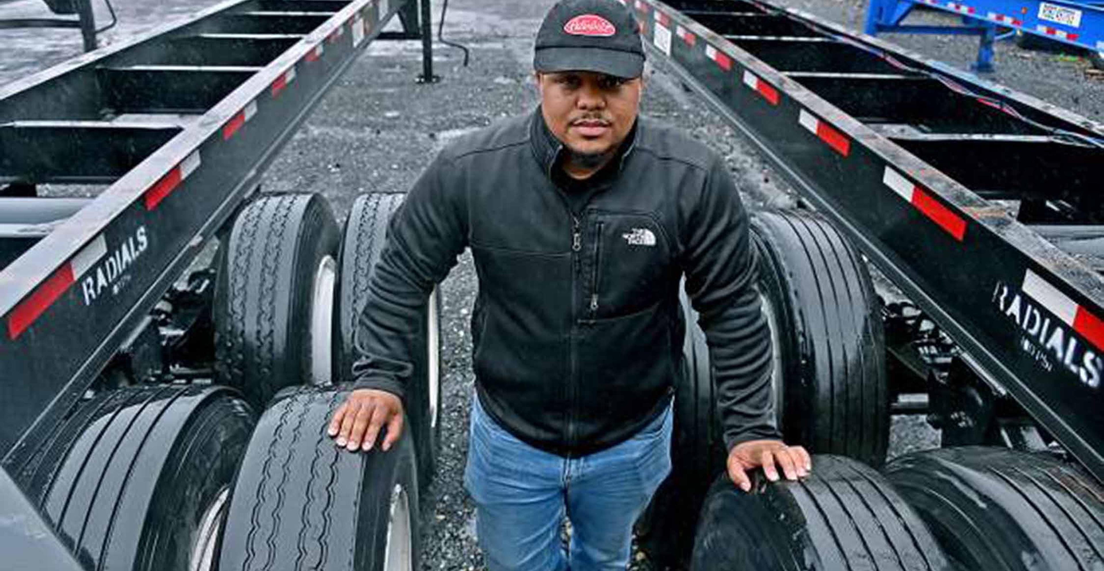 Truck driver standing in between the tires of a semi-truck.
