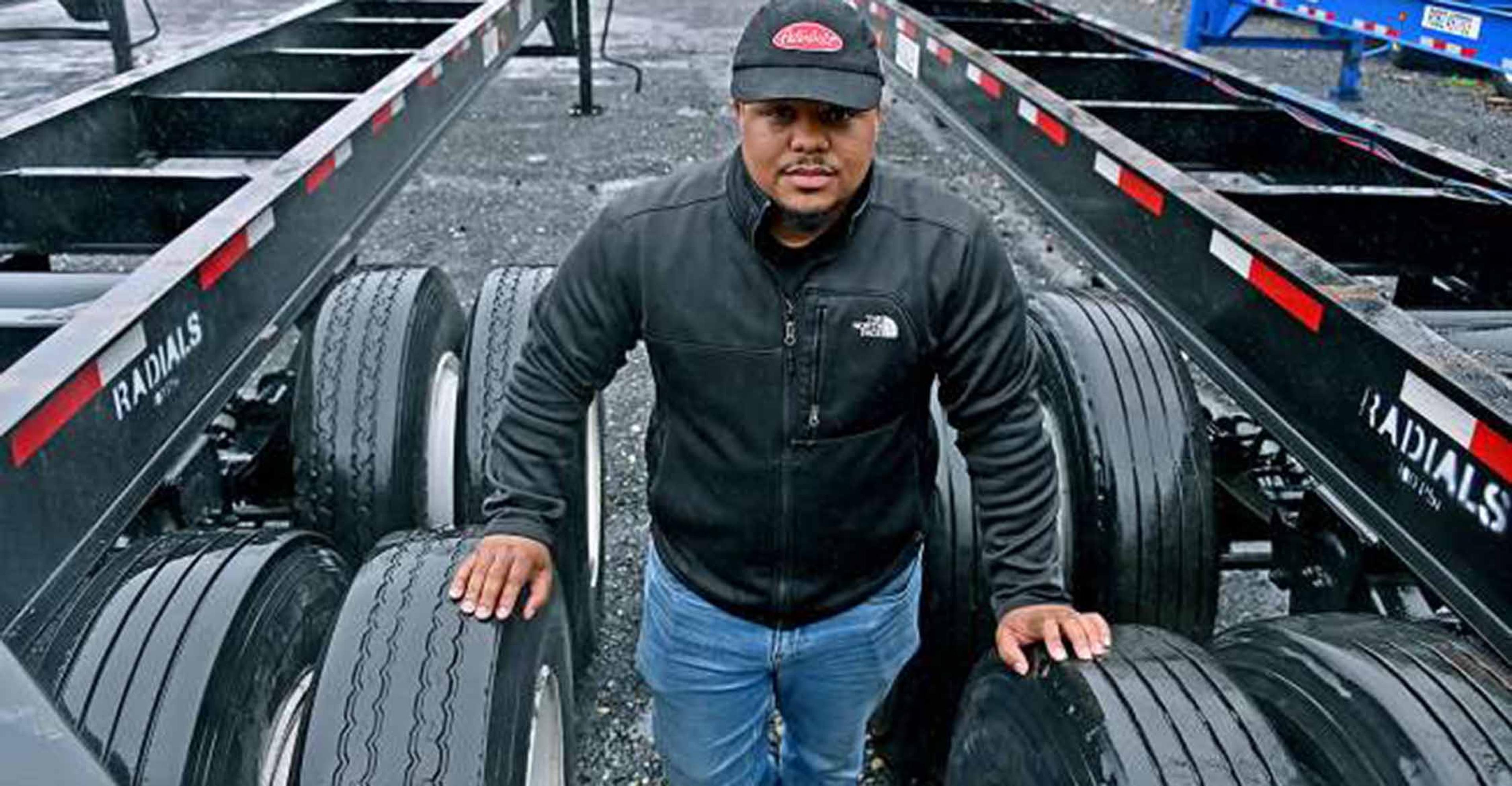 Truck driver standing in between the tires of a semi-truck.