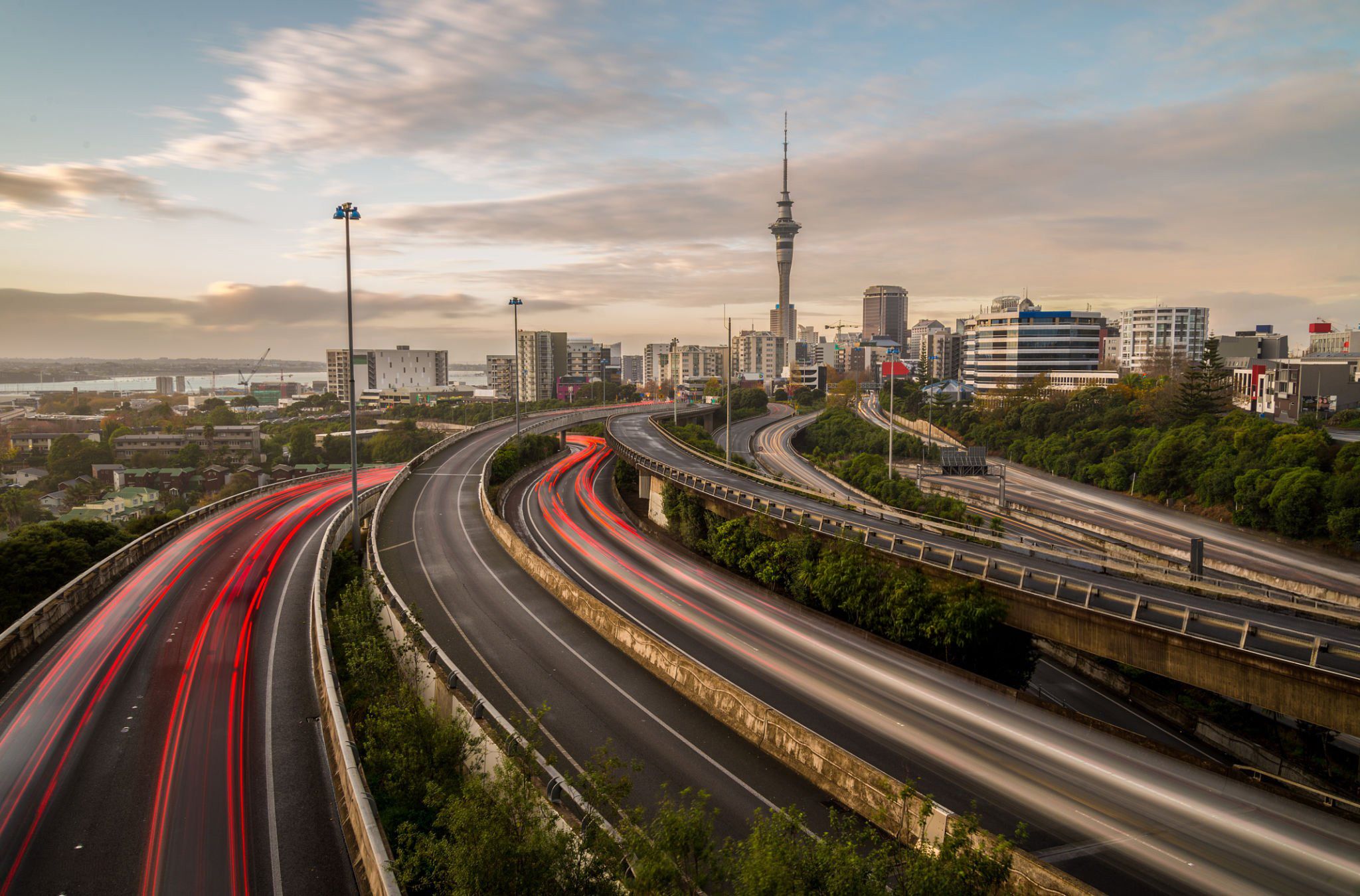Auckland motorway interchange at dusk, with light trails and the Sky Tower behind