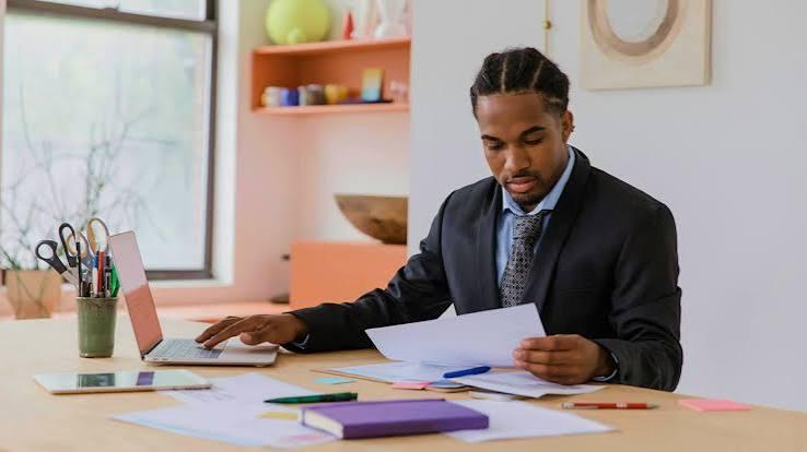 A business owner at a desk working through paperwork beside an open laptop.