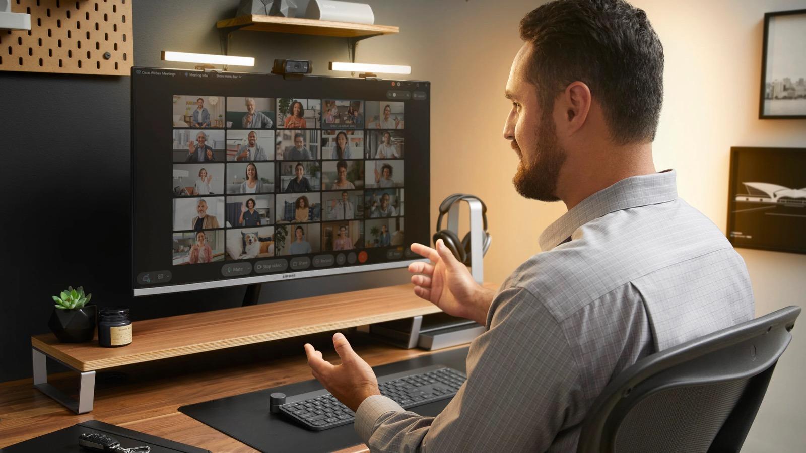 A professional at a home desk talking with a large team on a video call.