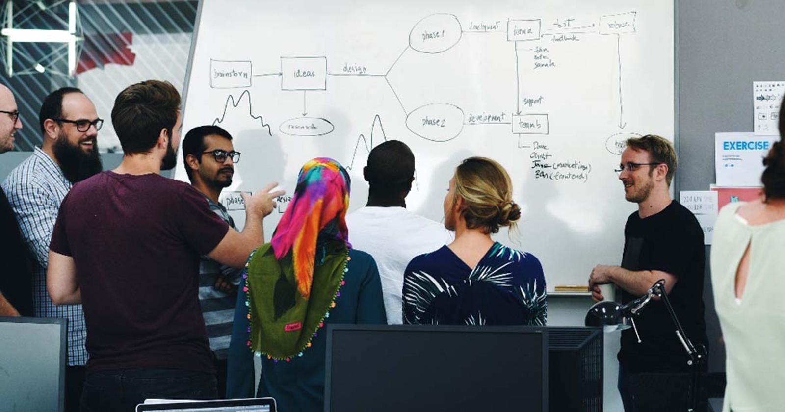 A team gathered around a whiteboard, mapping the phases of a project together.