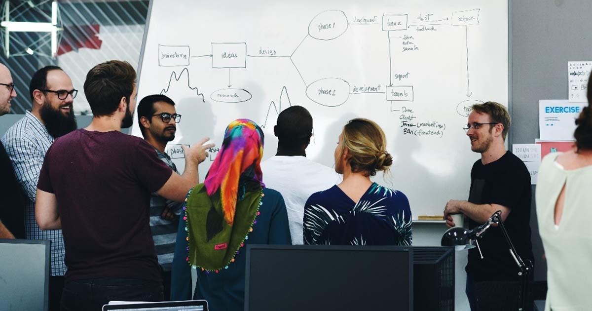A team gathered around a whiteboard, mapping the phases of a project together.