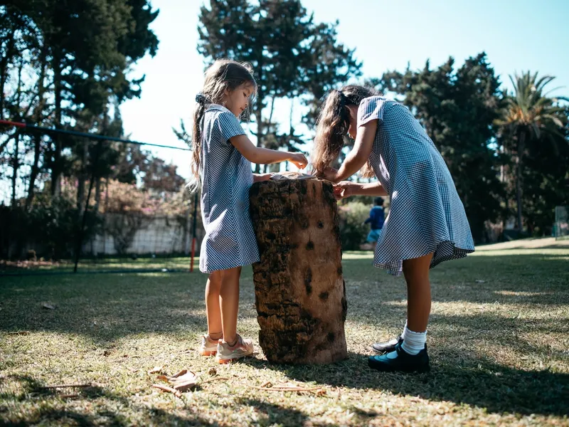two small girls playing together on log outside