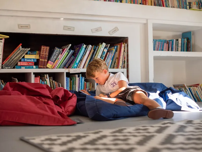 small boy reading book on bean bag in school library