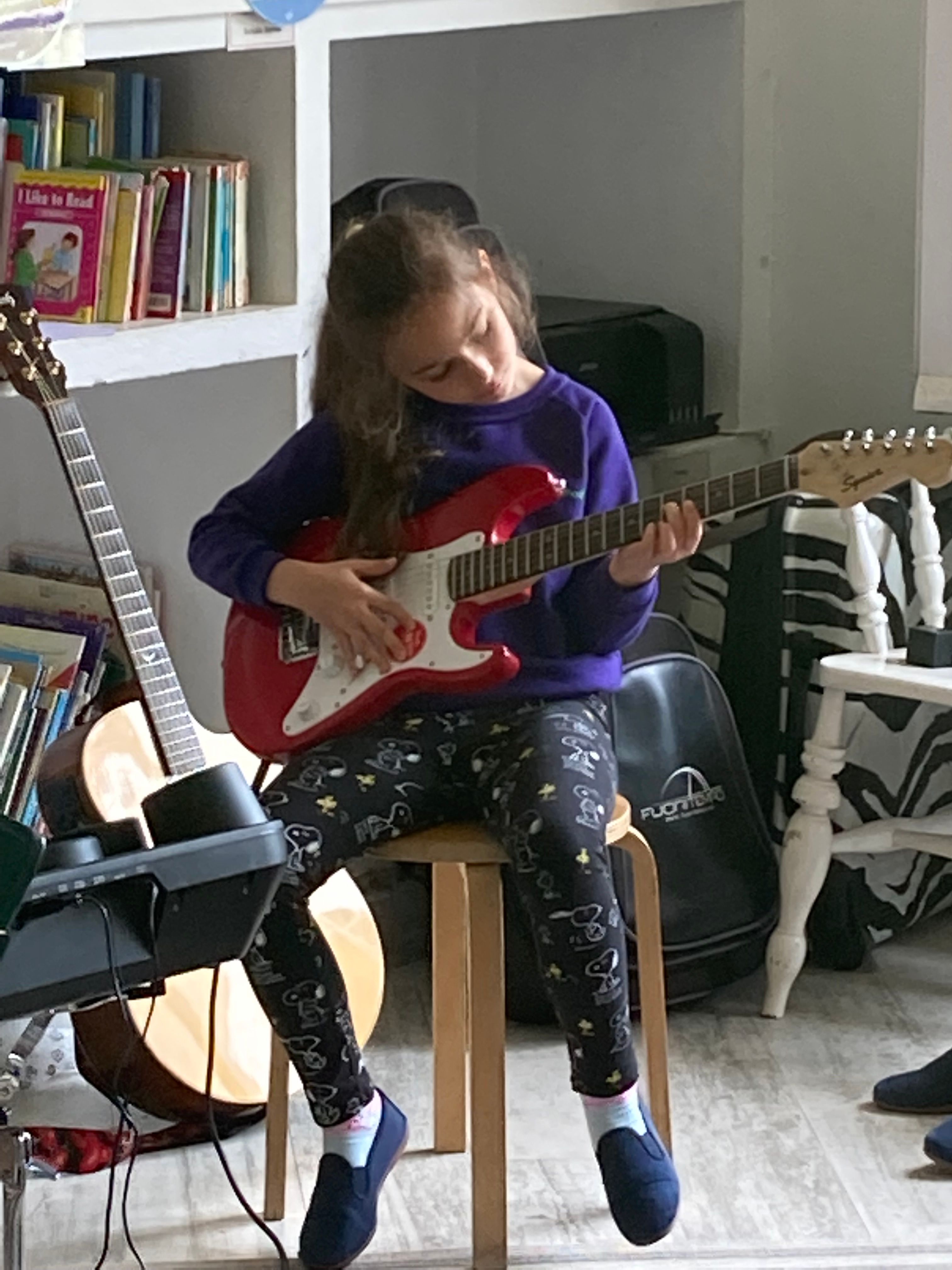 young school girl sitting on stool playing electric guitar