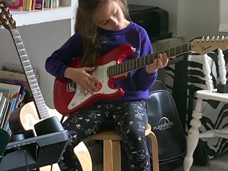 young school girl sitting on stool playing electric guitar