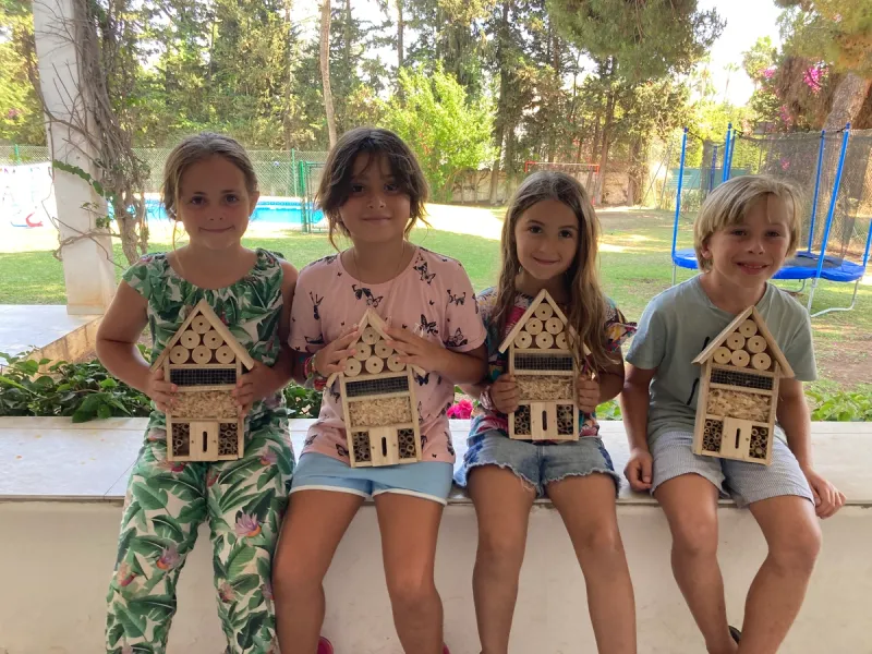 small children sitting on wall at summer school with bug houses