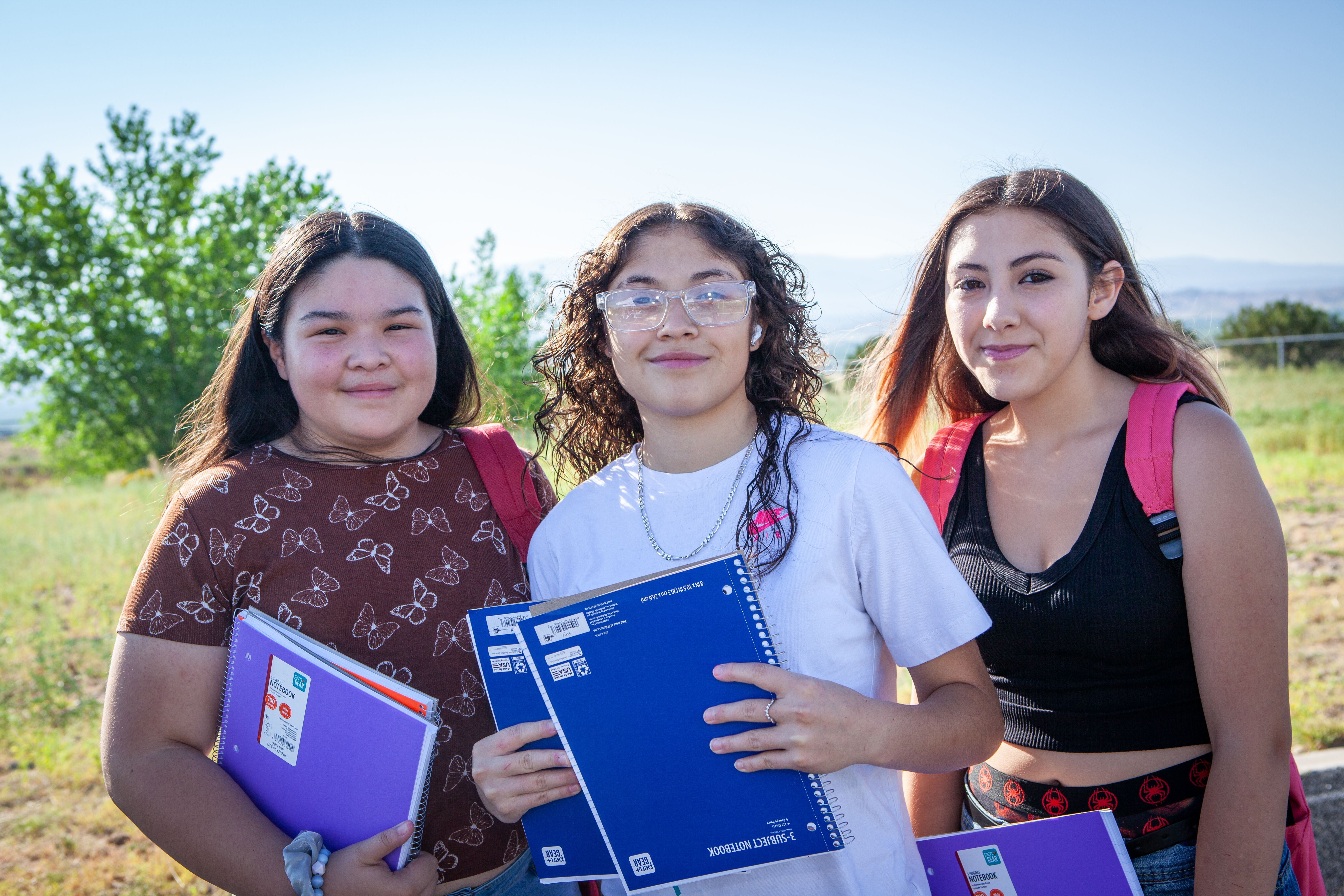 Three smiling students holding new school notebooks outdoors