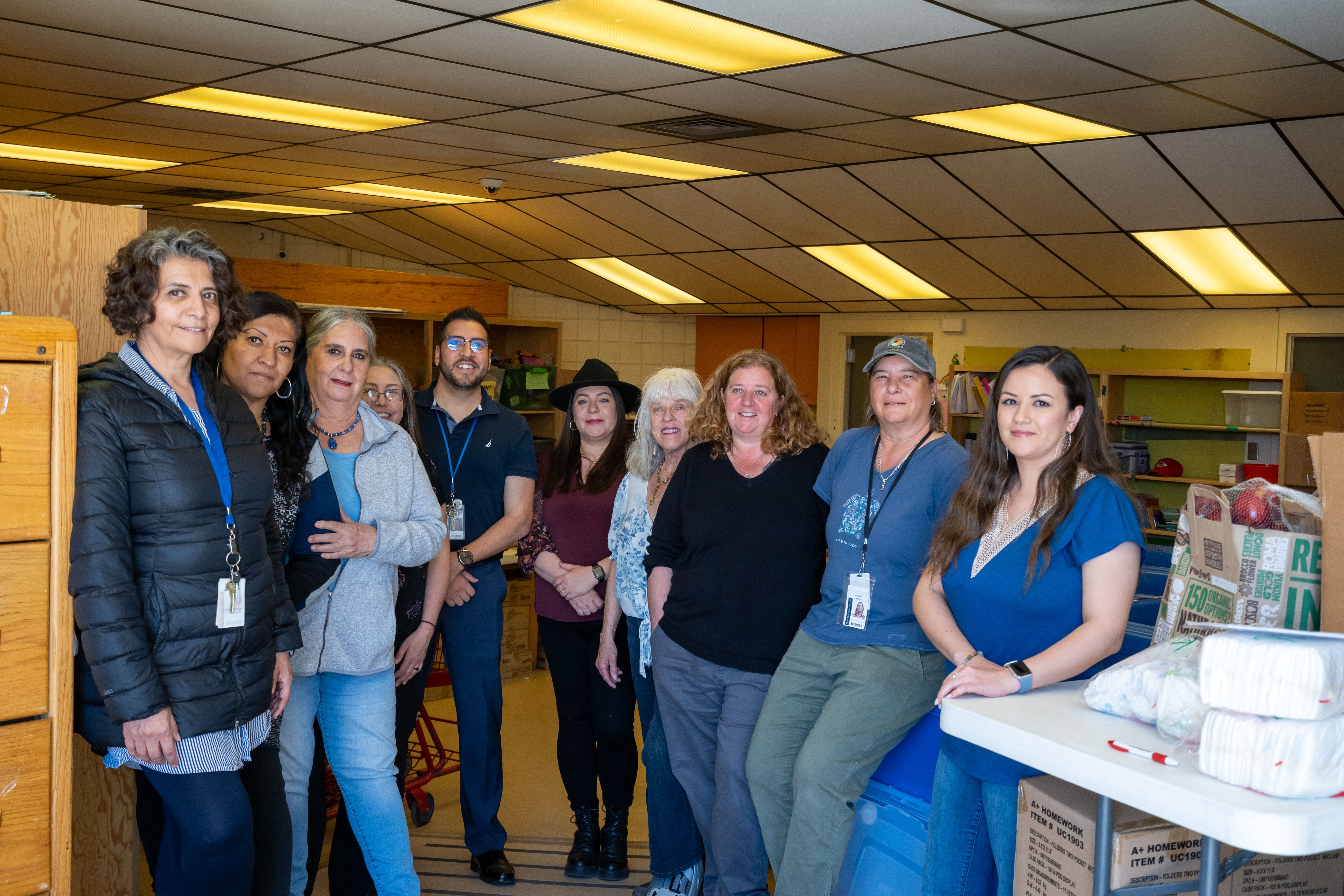 Adelante Program staff standing together in a supply room stocked with food, diapers and school supplies for Santa Fe students and families experiencing homelessness