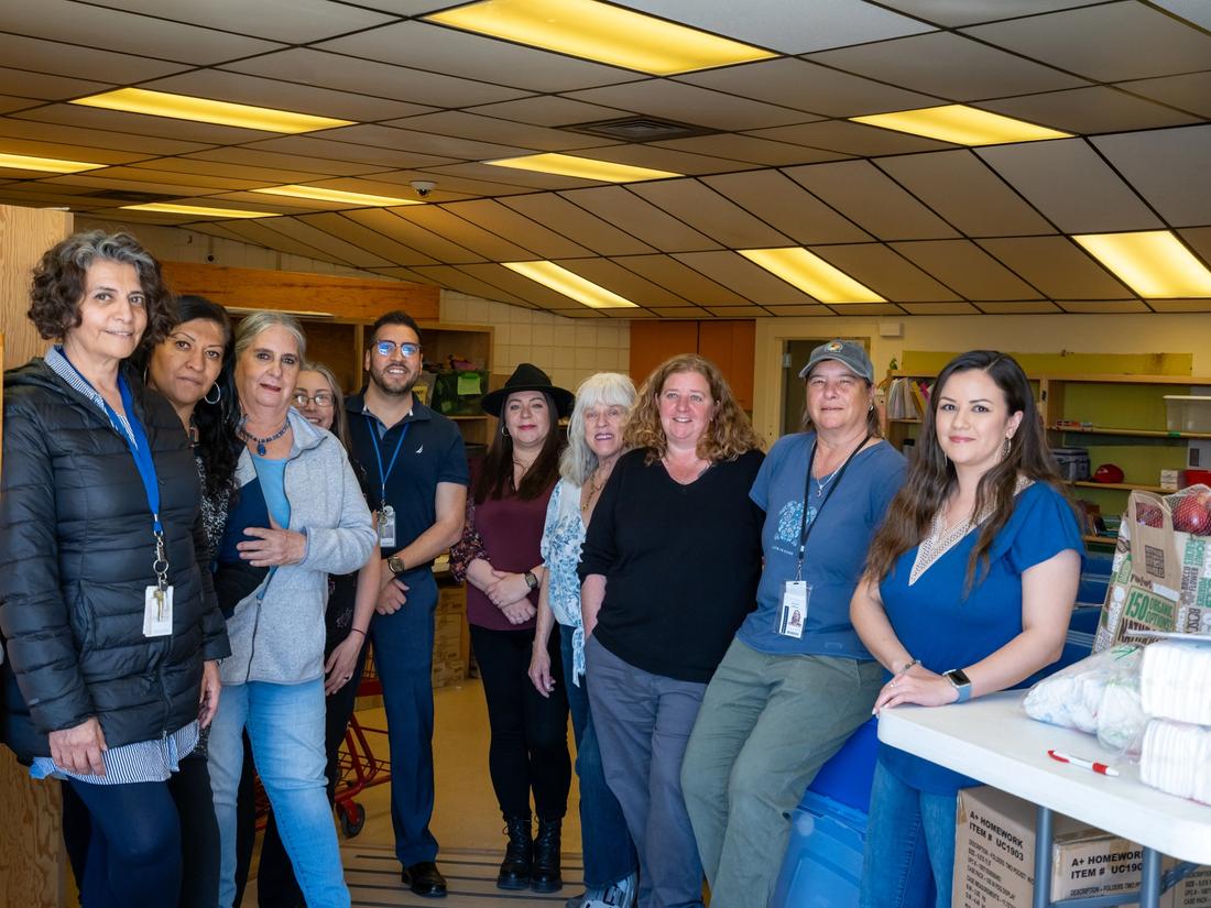 Adelante Program staff standing together in a supply room stocked with food, diapers and school supplies for Santa Fe students and families experiencing homelessness