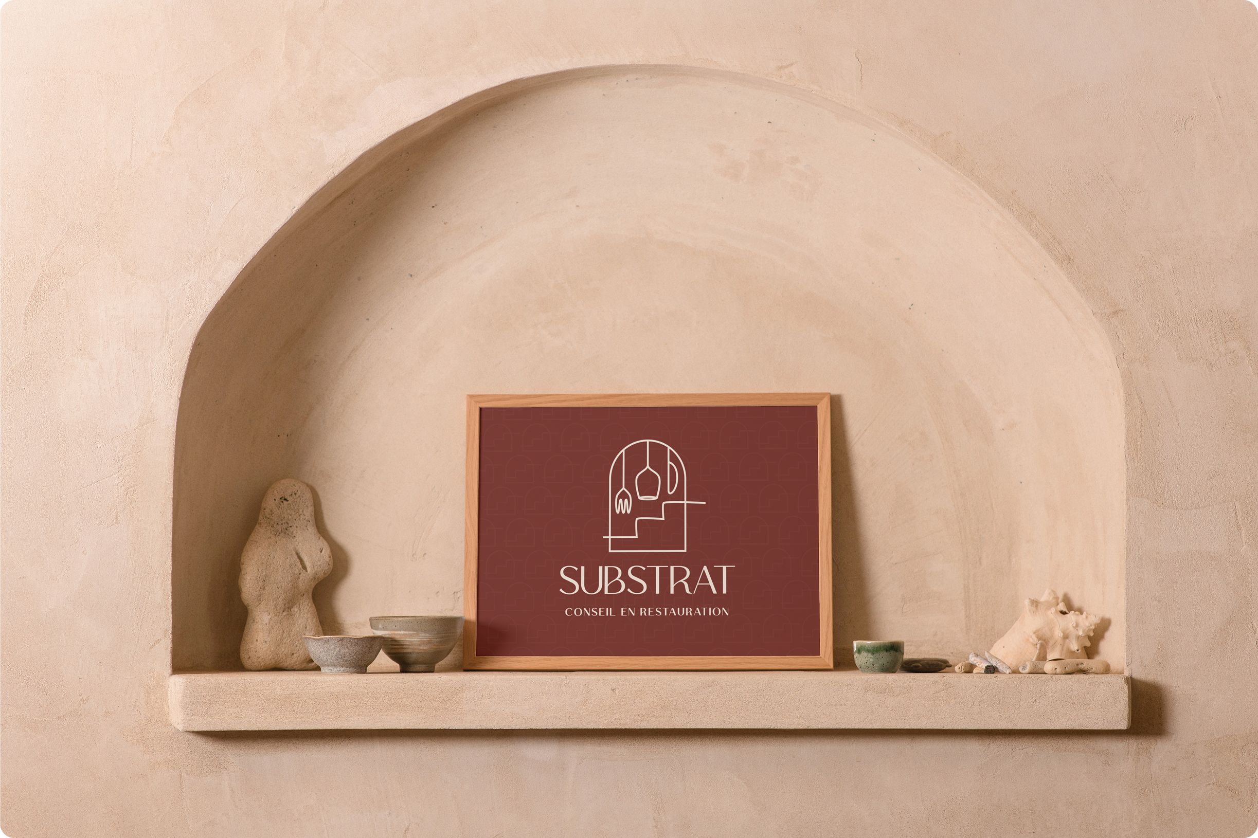 Logo de Substrat dans un cadre en bois à l'intérieur d'une arche murale avec des élements de décorations autour.