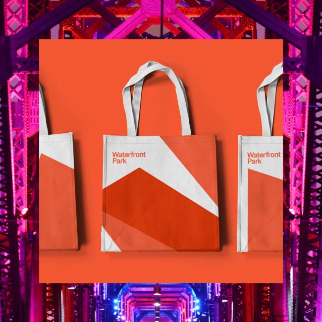 Waterfront tote bags on orange field on top of an image of the Waterfront Park Walking Bridge